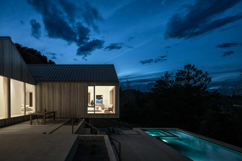 Modern Villa H with illuminated interiors and open patio next to a pool, set against a twilight sky with dark clouds.