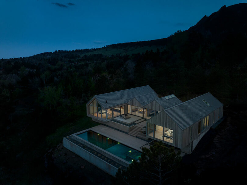 Villa H with illuminated interiors at twilight, nestled in a forested mountain area.