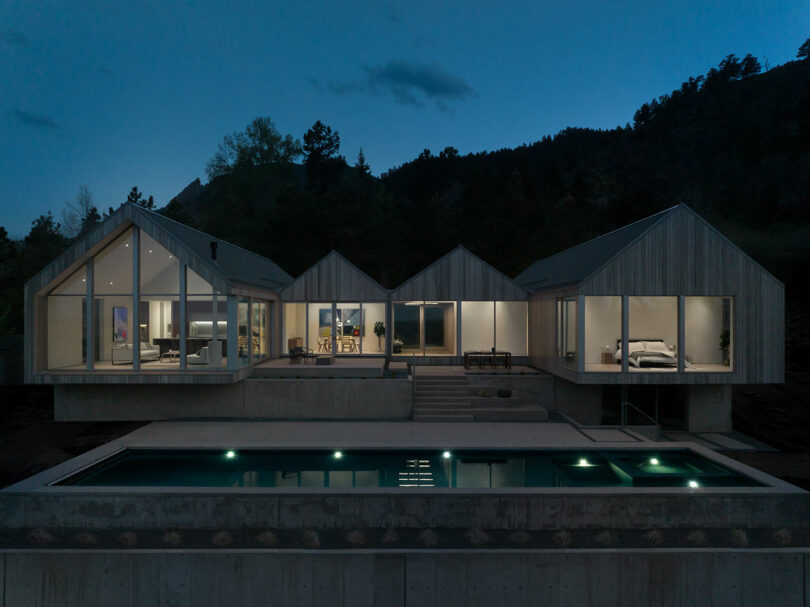 Villa H with large windows illuminated at twilight, showcasing interior rooms and a swimming pool in the foreground.