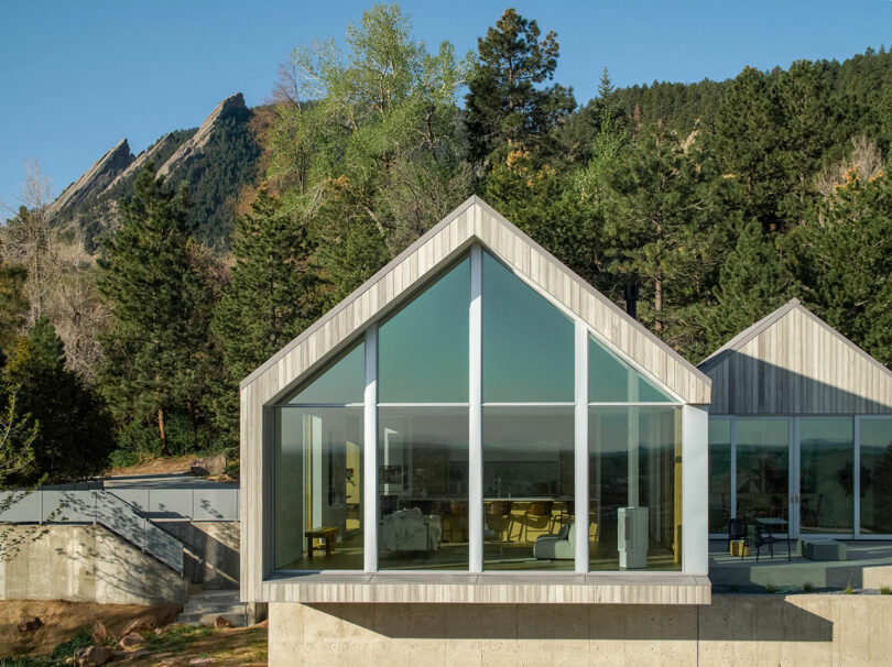 Modern Villa H with a triangular roof set against a backdrop of dense forest and rugged mountains.