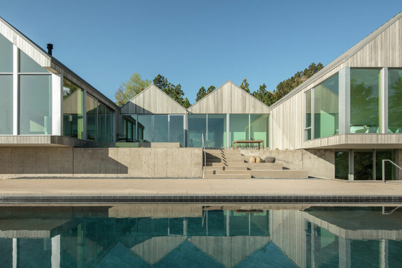 A modern architectural home known as Villa H, featuring triangular roofs and large glass windows, reflected in a calm swimming pool.