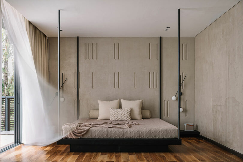 Modern minimalist bedroom with a low platform bed, textured gray walls, elegant thin black floor lamps, and a large window with white curtains.