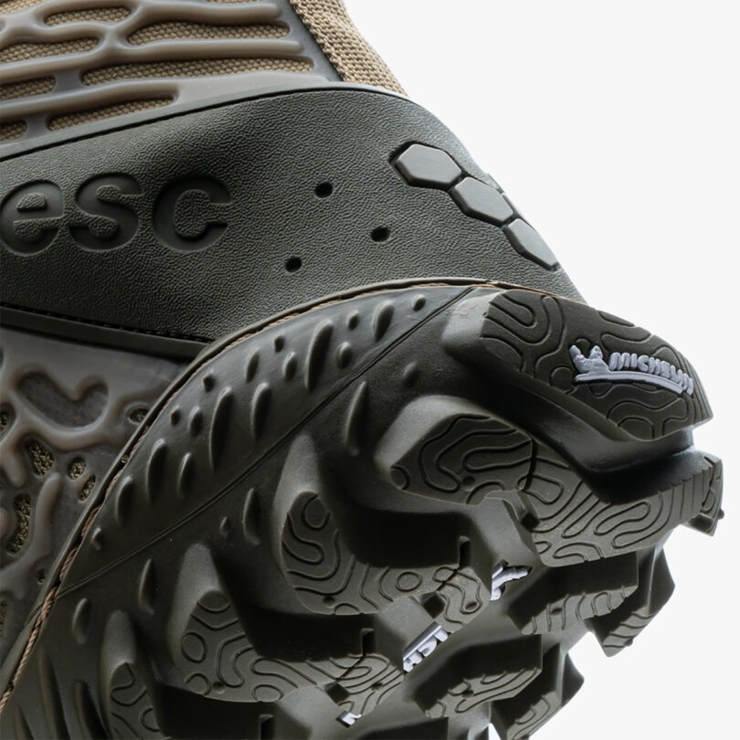 Close-up view of a Vivobarefoot Jungle ESC boot heel with intricate biomorphic designs on the sole and Michelin Man logo near the heel, highlighted by the label "esc" on a textured