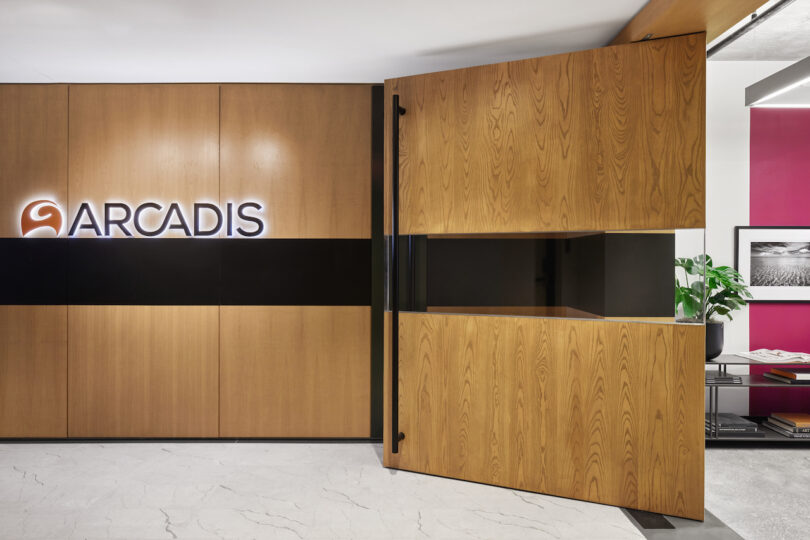 Modern office lobby with a wooden sliding door featuring the arcadis logo, contrasting sleek black panels and white marble floors
