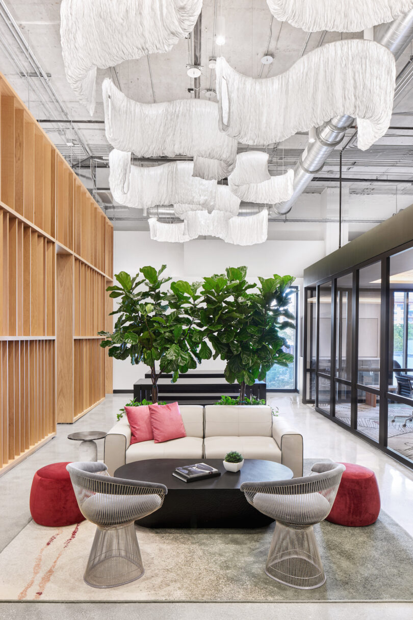 Modern office lobby with wooden walls, green plants, plush seating, and unique white light fixtures