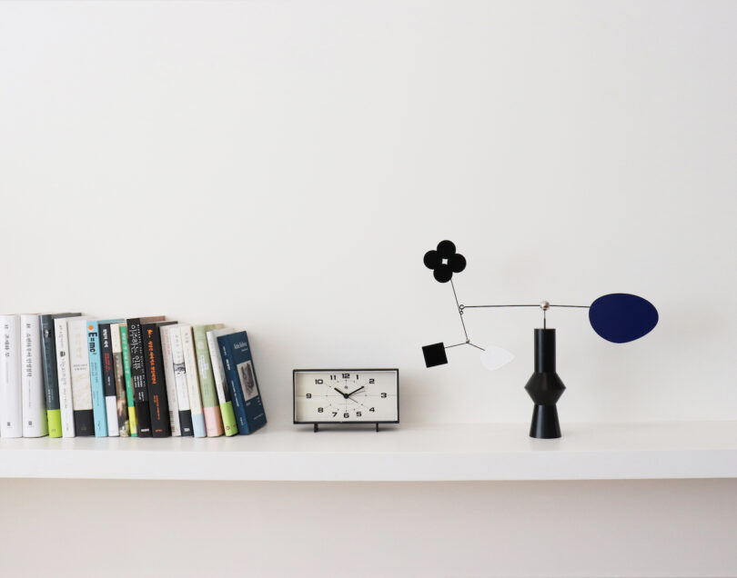 a desktop mobile with various shapes and a black base on a shelf next to books and a clock