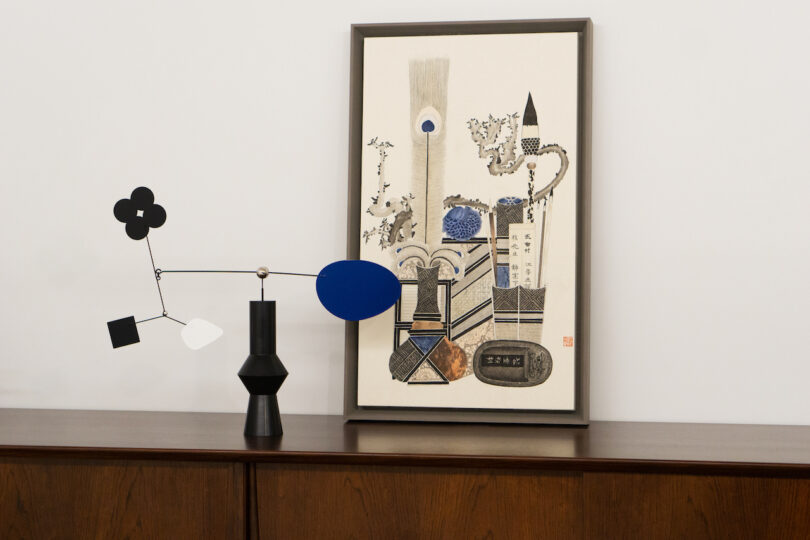 a desktop mobile with various shapes and a black base on a wooden console next to a framed piece of art