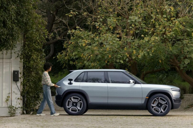 A person approaches a modern gray suv parked beside dense green shrubbery