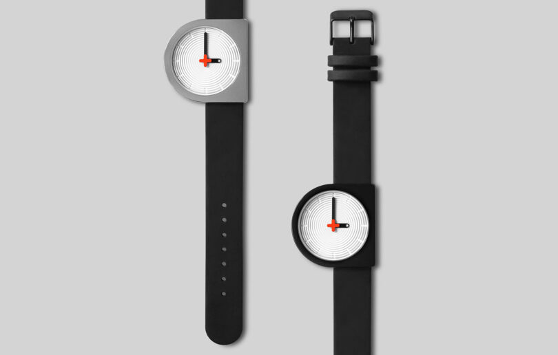 Two modern, minimalist D-shaped wristwatches with one black and one silver casing, each featuring a unique circular textured face and a single red watch hand.