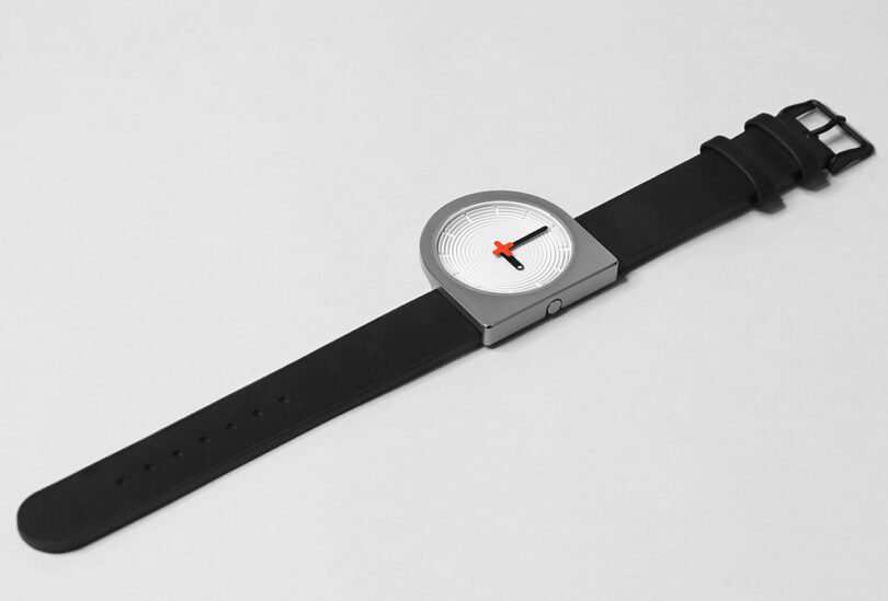 A minimalist D-shaped wristwatch with a silver case, unique concentric circle textured dial, and a black leather strap on a white background.