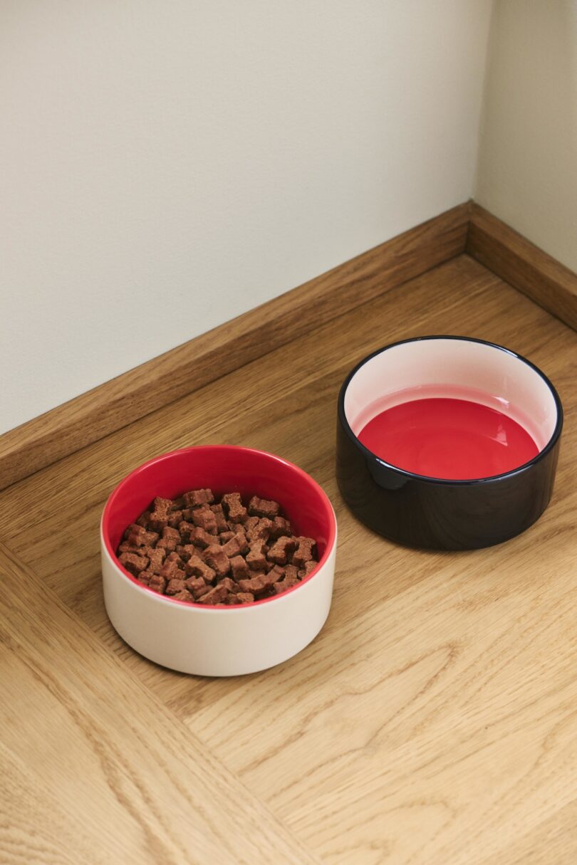 two white, red, and black dog bowls with food and water in them on the floor