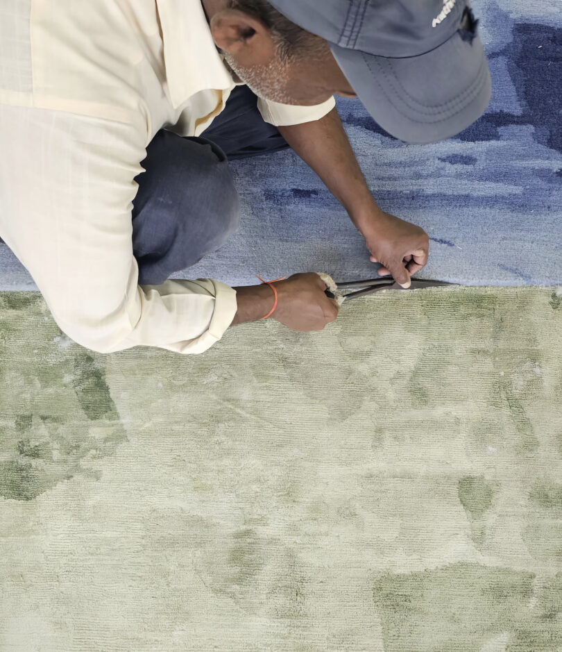 man cutting down the rug pile of a green and blue rug