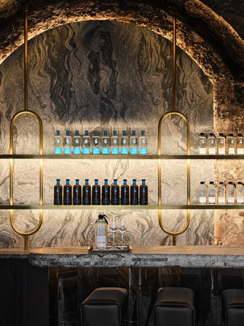 Stylish bar interior with illuminated shelves displaying rows of Casa Dragones bottles against a textured marble backdrop.
