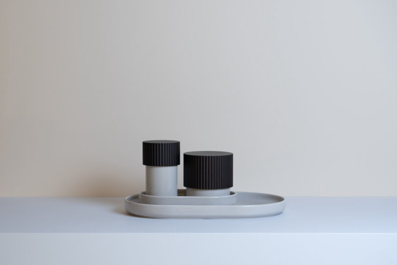 two storage boxes with black tops on a tray on a grey table
