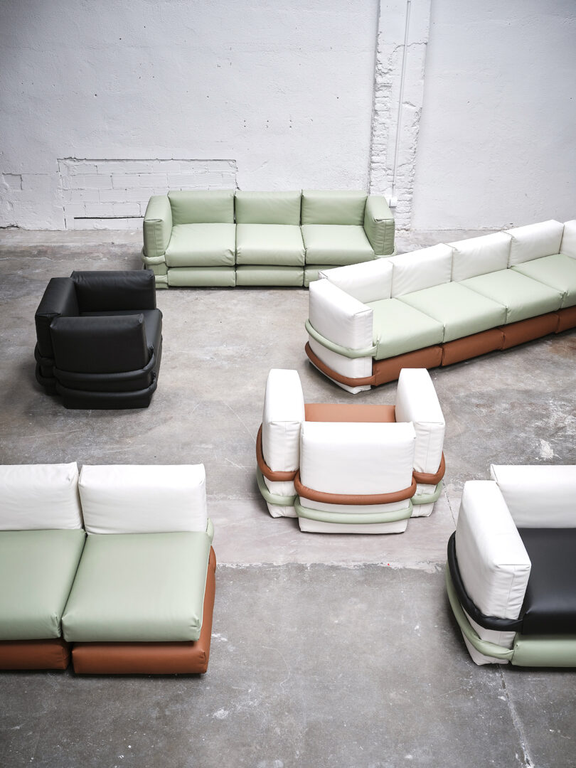 Several modern modular sofas in various colors arranged in a spacious room with white walls and a concrete floor.