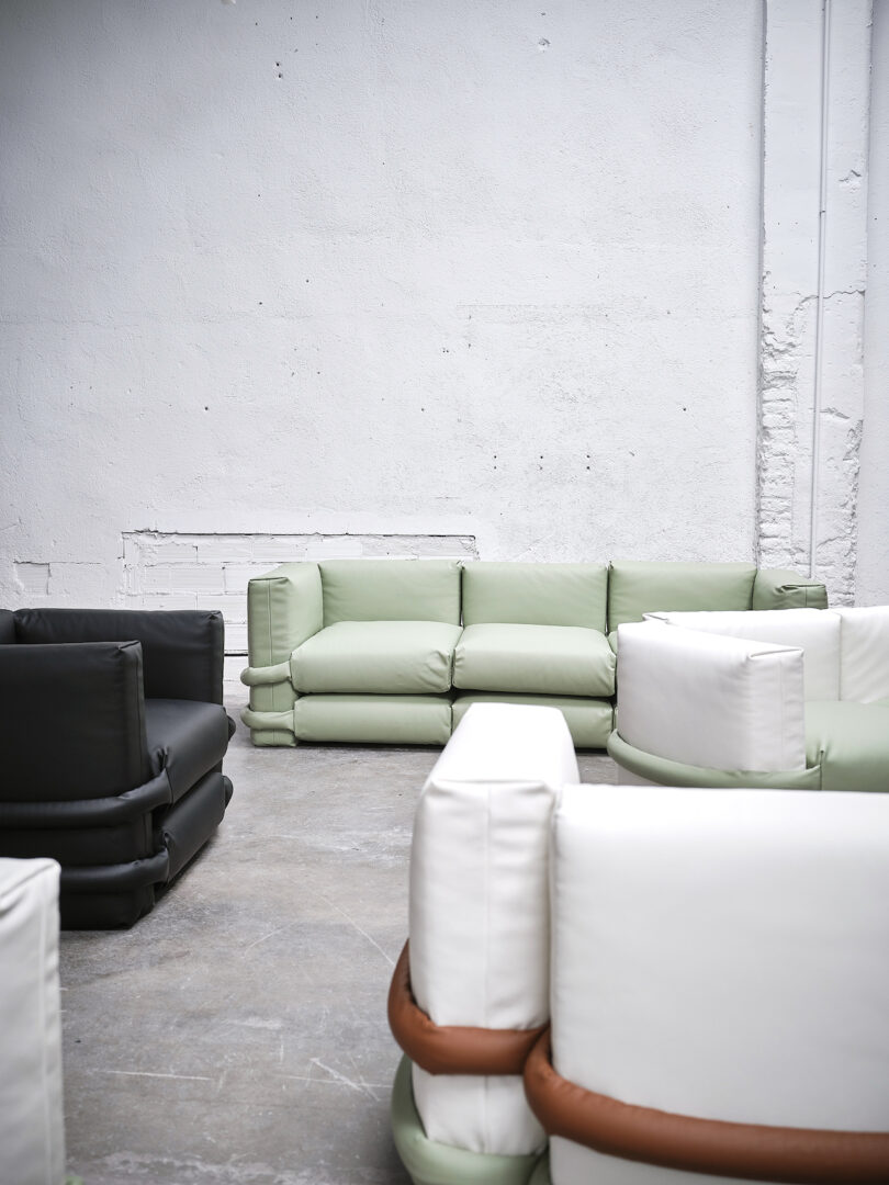 An arrangement of modern sofas in black, white, and mint green placed against a white textured wall in a minimalist setting.