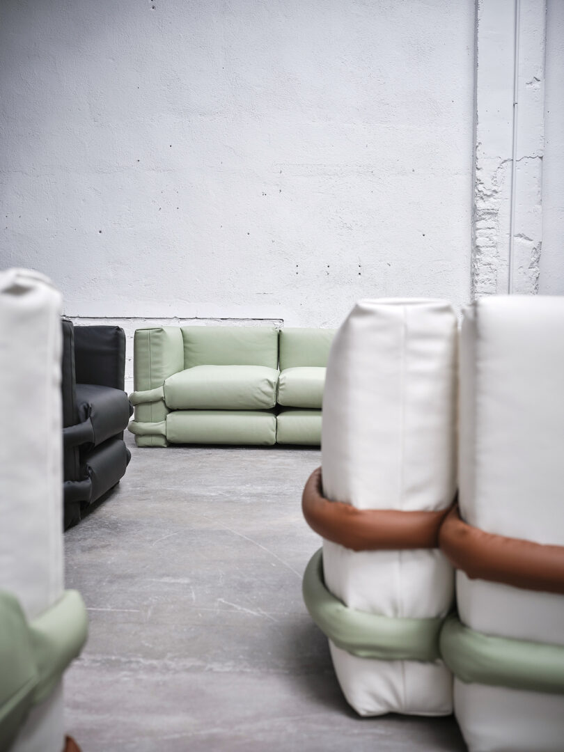 An assortment of modern sofas in black, white, and mint green placed against a white textured wall in a minimalist setting.