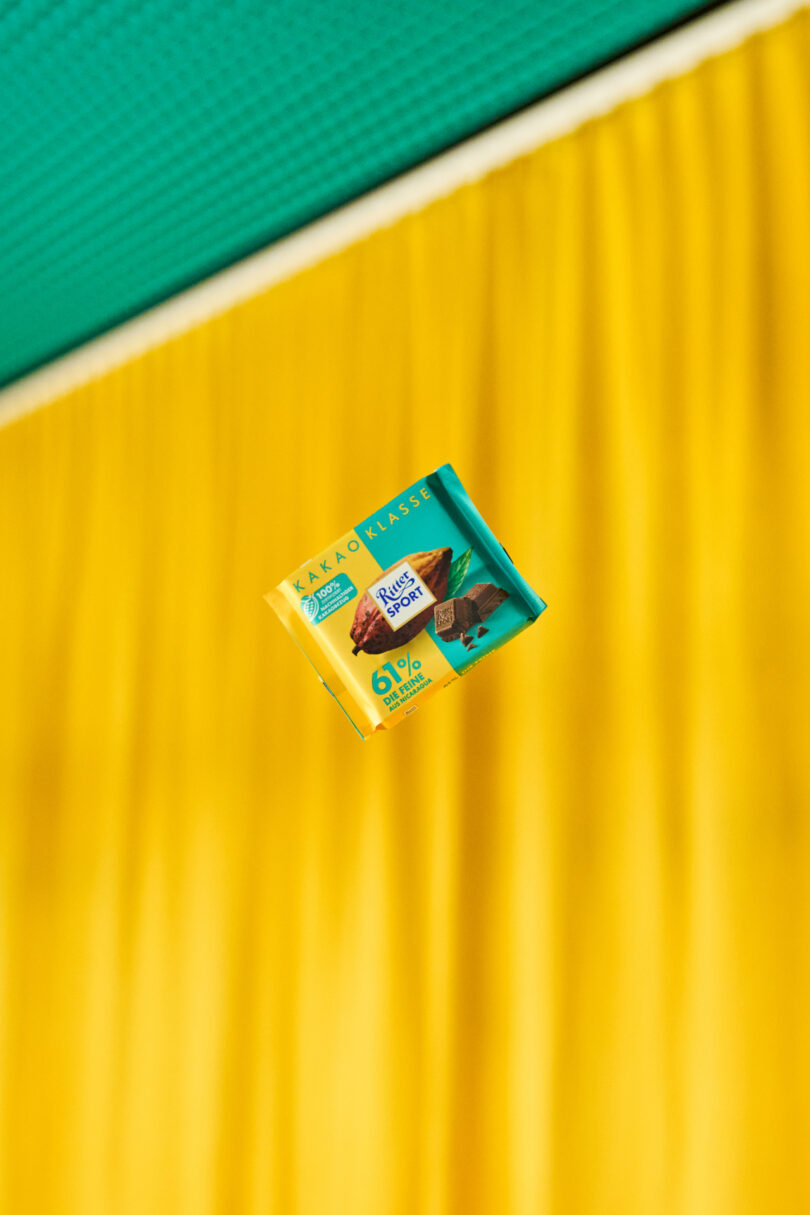 a chocolate bar suspended in the air against a yellow corrugated background with a green edge visible at the top.