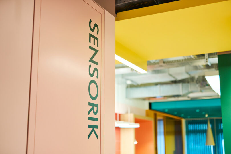 Modern office interior with colorful ceiling and a doorway labeled "sensorik.