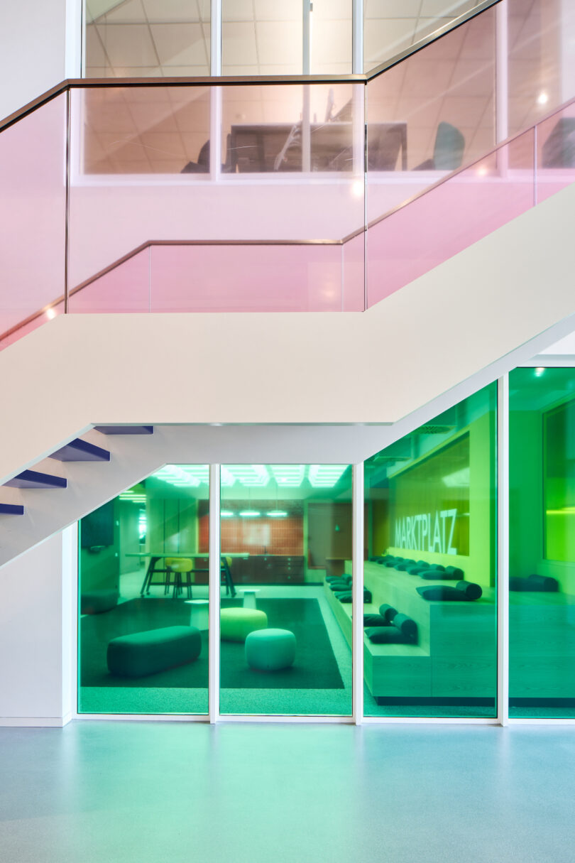 Modern office interior featuring a staircase with color accents and a glass-walled meeting room with green lighting and the word "marktplatz" on the door.