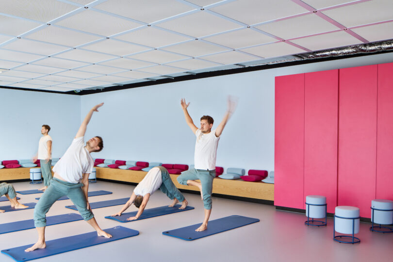 People practicing yoga in a modern studio with a pink accent wall.