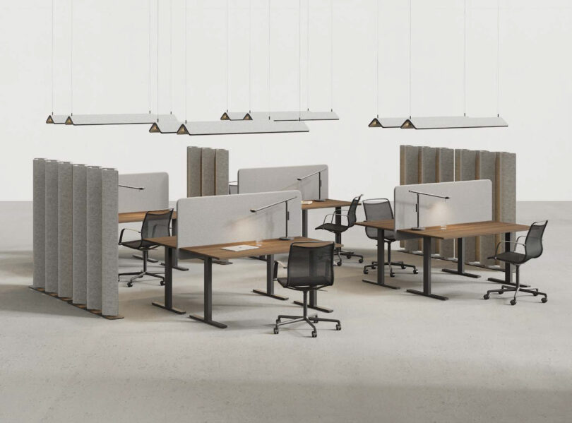 Modern office space with rows of desks, partition panels, and suspended rectangular lights in a minimalist setting.