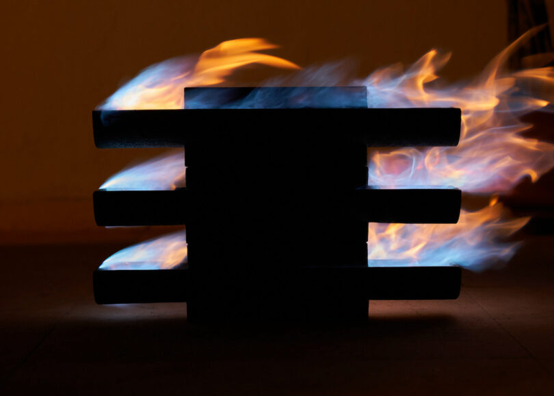 flames surrounding a black three-tiered object against a dark background.