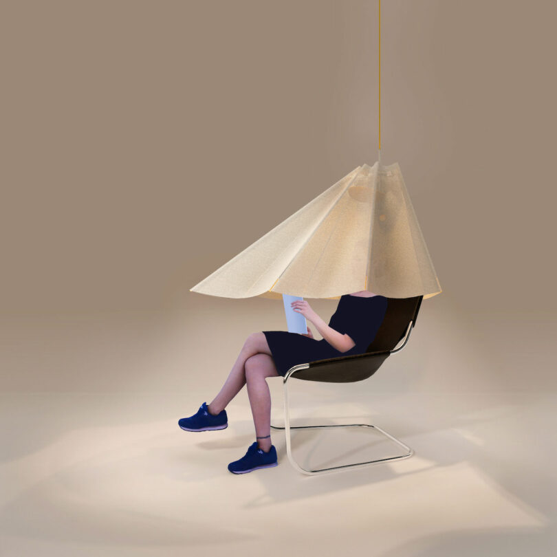 A person seated in a modern chair, reading a book under an oversized, conical pendant light.