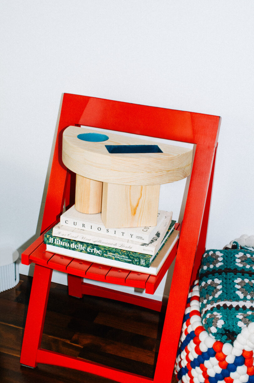 wood side table with colorful geometric cut outs on a stack of books on a red chair