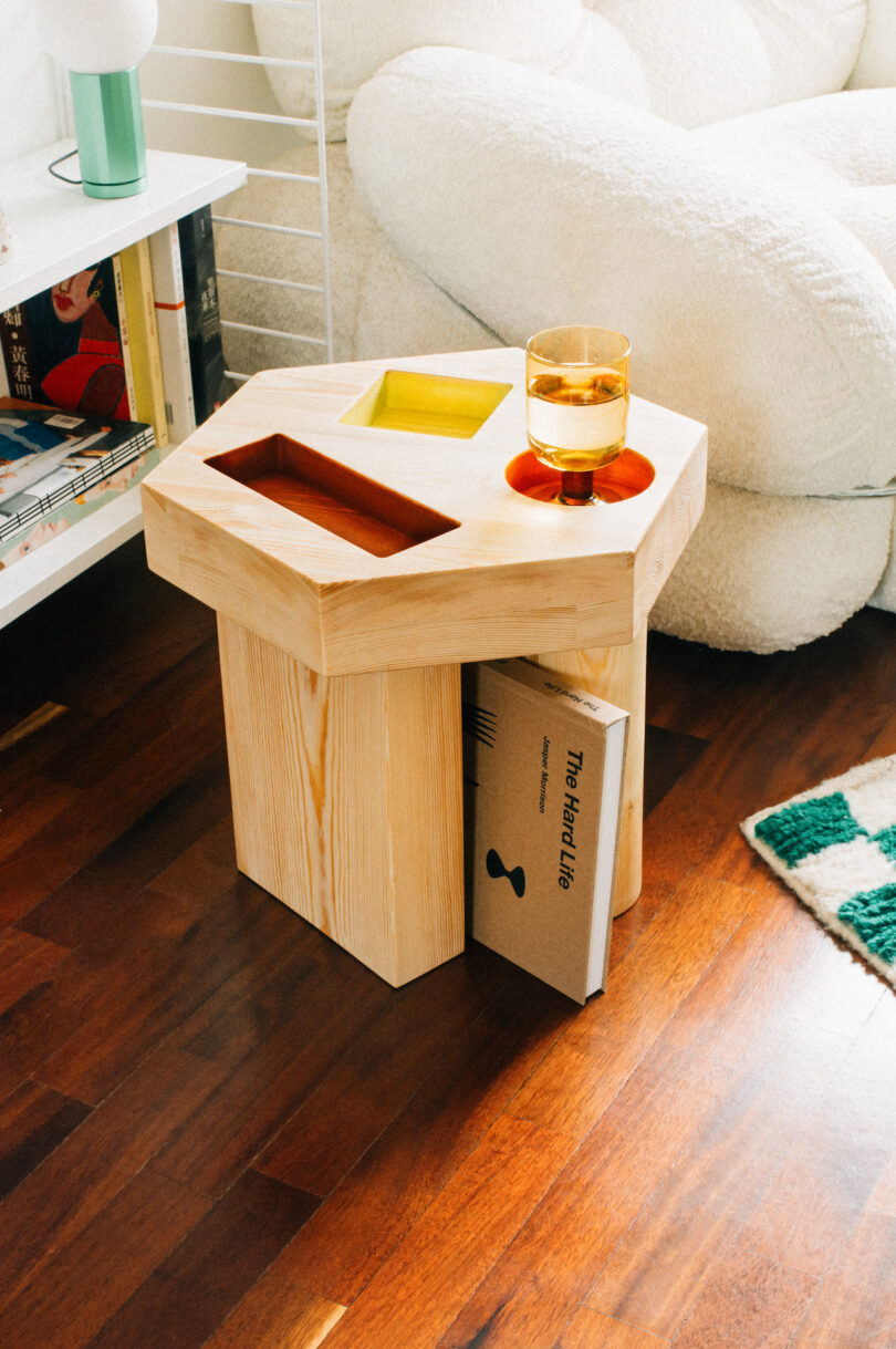 A modern wooden side table displaying colorful books and a glass of tea, placed beside a cozy white armchair in a living room