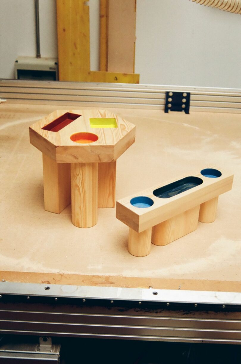 two wood side tables with colorful geometric cut outs on a work bench