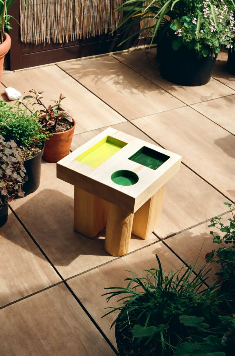 wood side table with colorful geometric cut outs outdoors next to potted plants