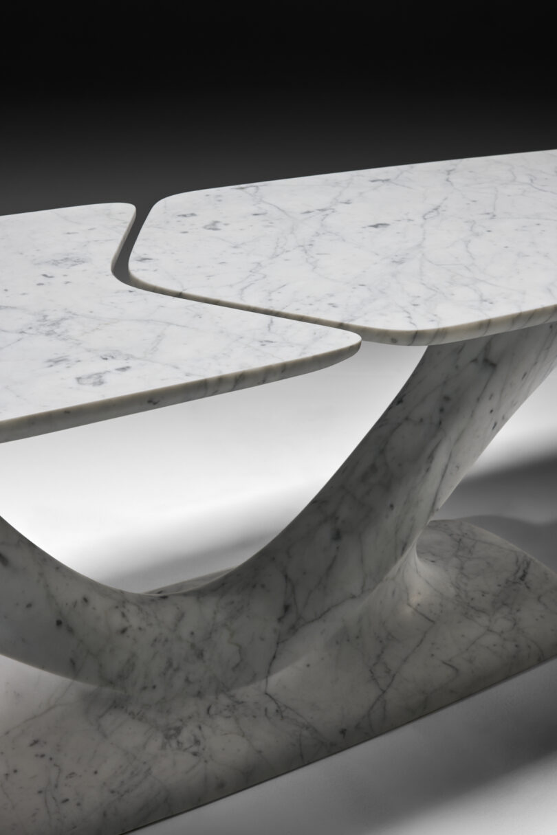 up close details of a modern marble table with a unique v-shaped base and a split, elongated oval top, highlighted against a black background.