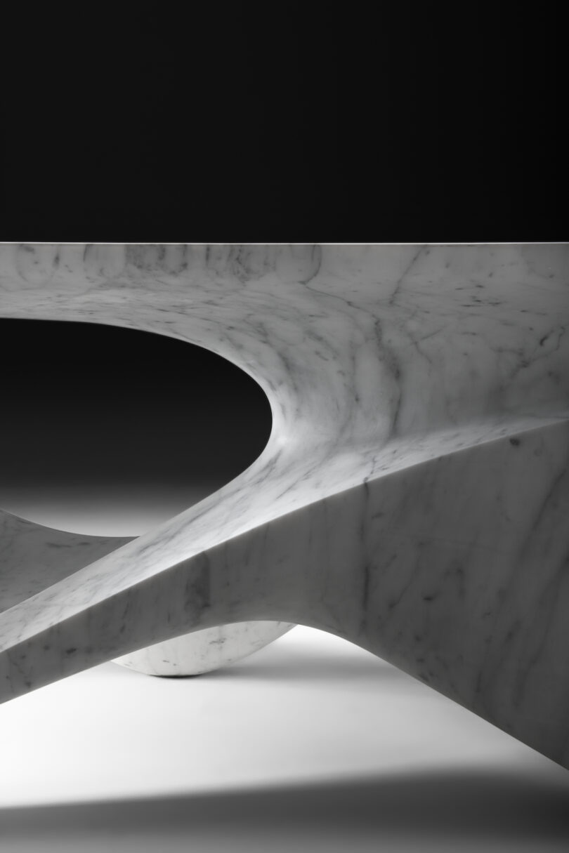 up close details of a sleek, modern marble sculpture with a symmetrical, eye-shaped hollow center, displayed against a shadowy background