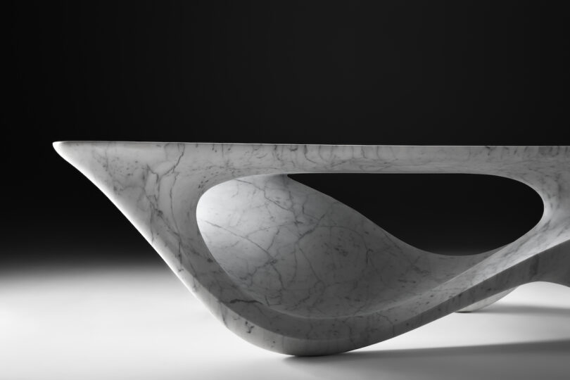 up close details of a sleek, modern marble sculpture with a symmetrical, eye-shaped hollow center, displayed against a shadowy background