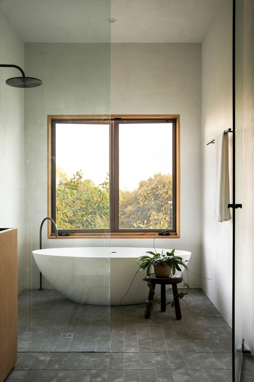 View in a minimalist modern bathroom through an open glass shower door into a shared space with a floating bathtub and shower with a window behind.