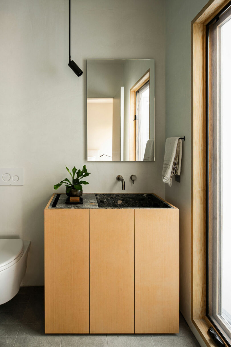 Partial view of a modern bathroom with a minimalist wooden sink cabinet with a marbled inset sink bowl.