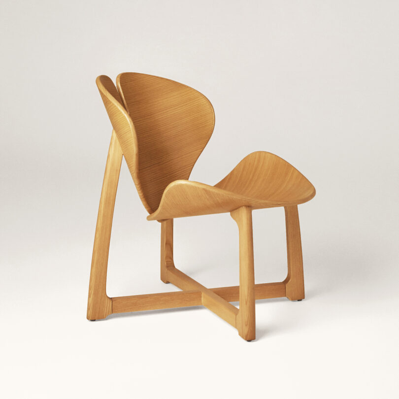 A wooden chair featuring a modern, sculptural design with a prominent, curved backrest and a smaller, connected side seat, set against a plain background