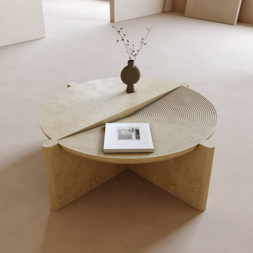 Modern round coffee table made of textured material, featuring a rotating top with ribbed pattern, a vase with branches, and a magazine, placed in a minimalistic room with beige flooring