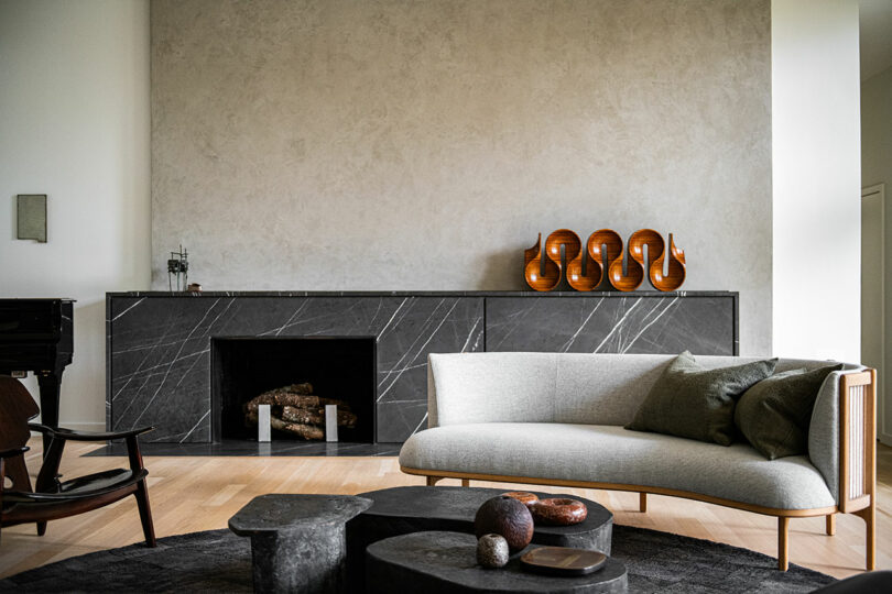 Modern living room with light grey couch, black marble fireplace, abstract decor, and wooden accents, exuding a touch of Brazilian Modernism. Decorative wooden ornaments are displayed on the mantel.