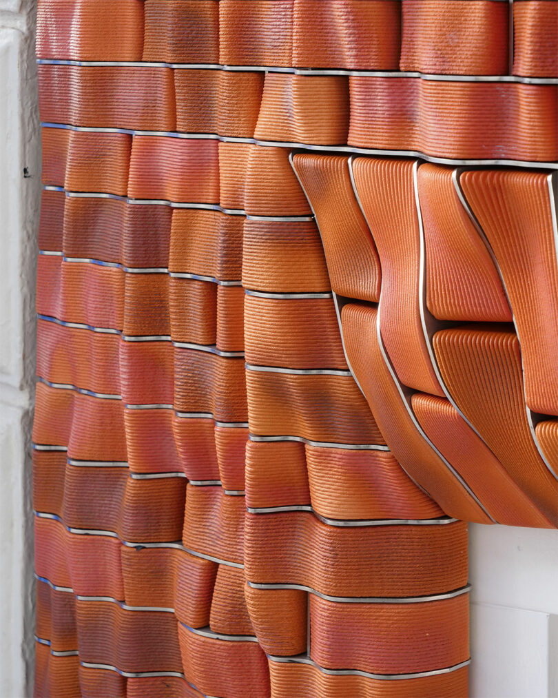 Close-up of a textured wall with an elaborate pattern of overlapping orange ceramic tiles, creating a dynamic, wavy surface.