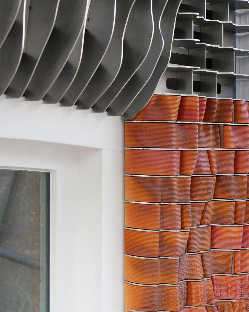 Close-up of a building corner showing contrasting textures: smooth white window frame, wavy metal siding, and orange textured tiles.
