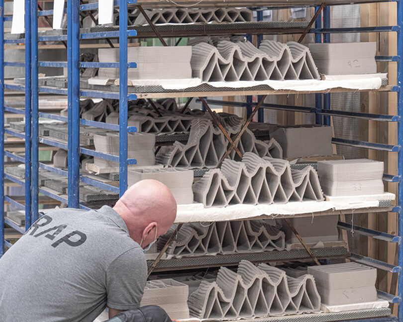A worker examines ceramic molds stored on multiple shelves in a warehouse.