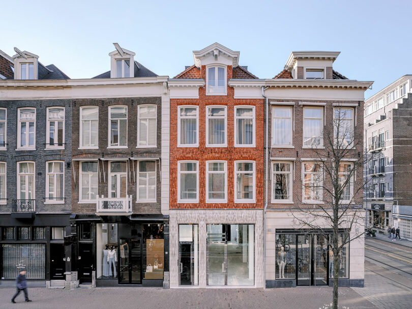 Facade of three adjacent european townhouses with traditional architecture, featuring ground floor shops and upper residential stories, on a sunny day with a clear sky.