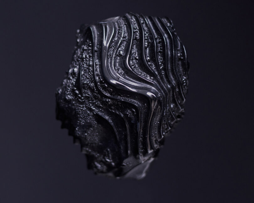 Close-up of a black object with intricate, wavy patterns on a dark background.