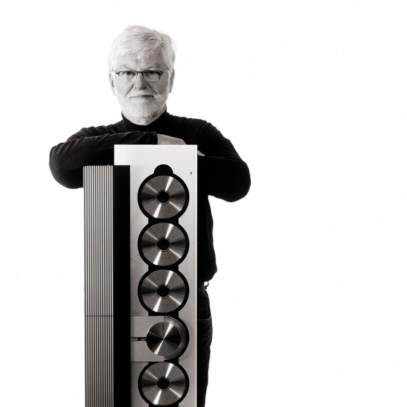 Black and white photo of David Whitfield Lewis standing behind the original vertically oriented Beosound 9000 CD player he designed.