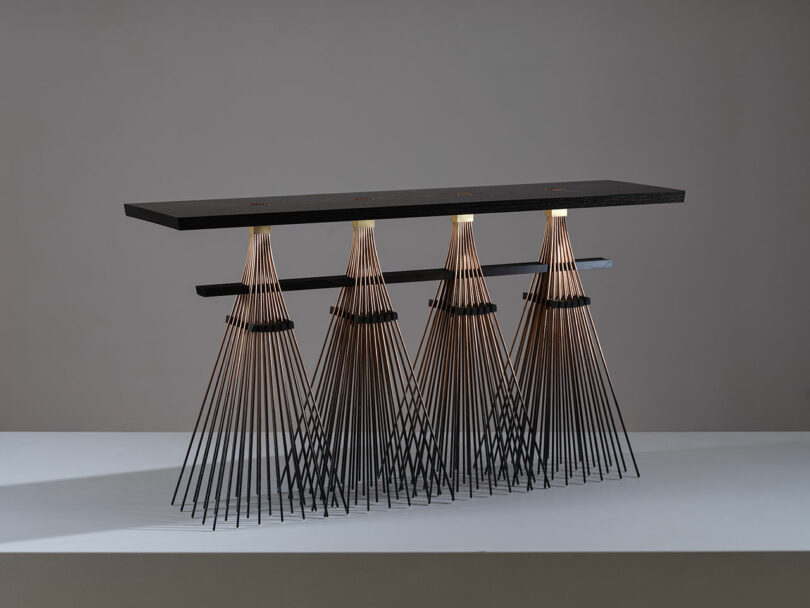 A modern table featured at Design Miami with a black top supported by intricately designed conical black metal legs resembling inverted lampshades.
