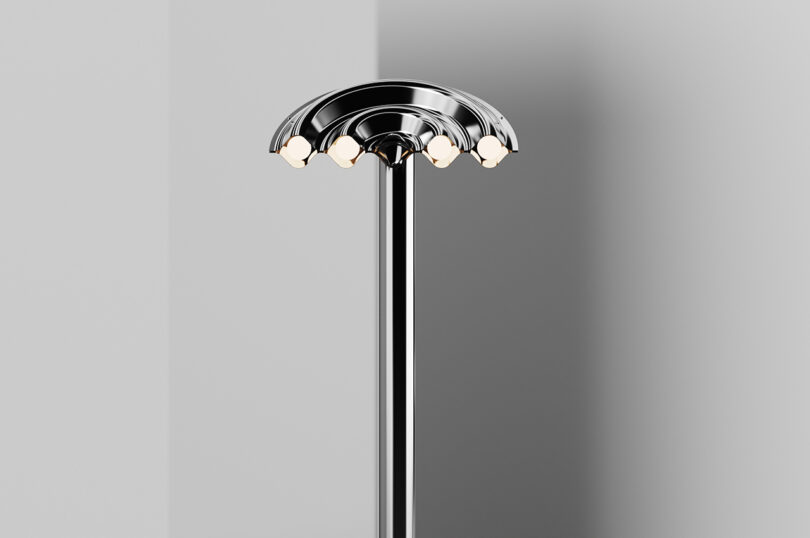 A modern, silver floor lamp with multiple bulbs arranged in a semi-circular pattern at the, positioned against a gray wall.