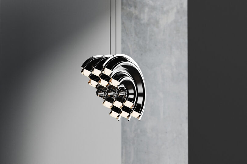 Uma moderna luminária suspensa metálica com múltiplas camadas em arco, pendurada sobre um fundo cinza.