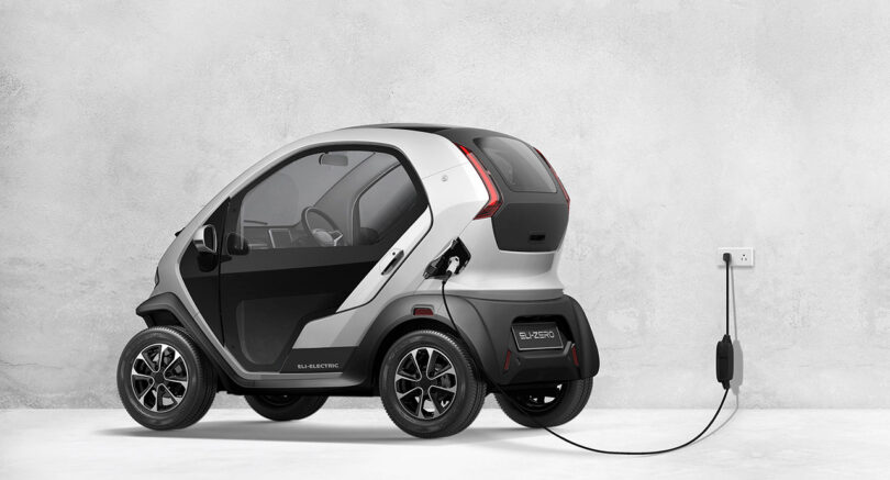 Compact micro EV, Eli ZERO, plugged in and charging, parked against a plain gray background.